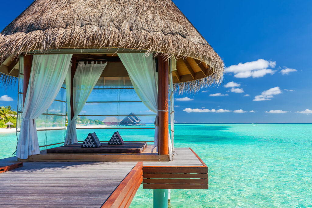 Bungalow di Lusso a picco sul mare limpido delle maldive. Il tetto è in legno e paglia, e dalle tende si vede un materassino: tutto pronto per una vacanza all'insegna del relax