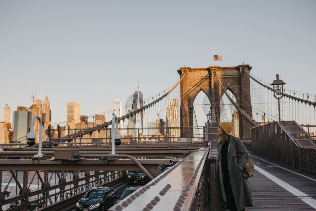 una donna guarda il fiume Hudston dal Manhattan Bridge. Si vedono le campate del ponte, la parte pedonale e i grattacieli in lontananza